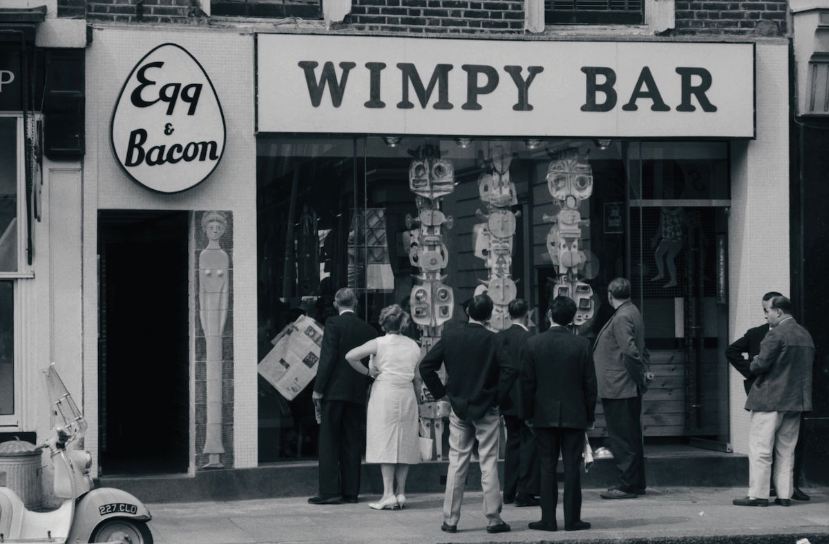 Passers-by looking at a modern sculpture in the window of a Wimpy Bar in London, c.1961. Photograph by John ‘Hoppy’ Hopkins. © Estate of John Hopkins.